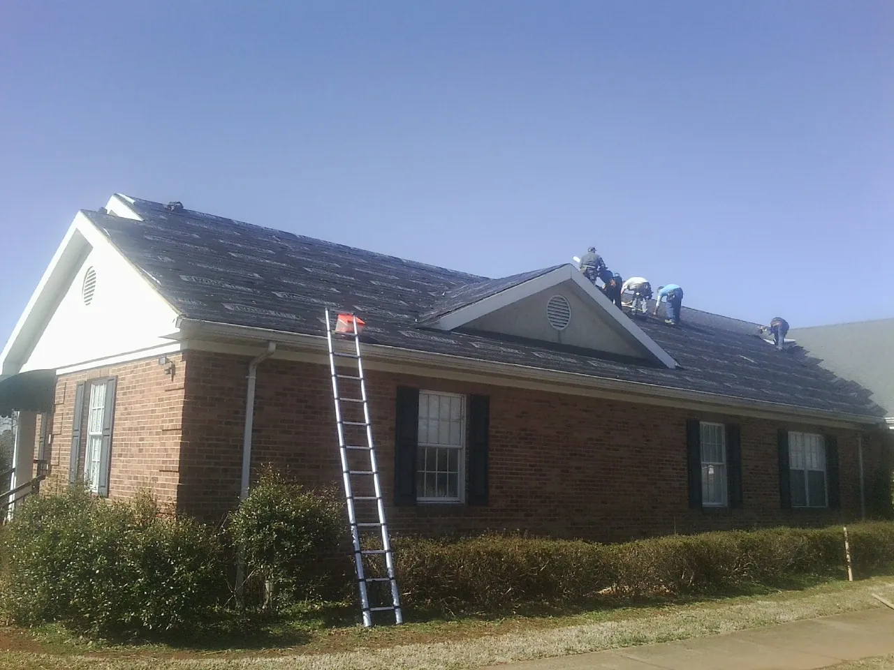 Crew tearing shingles off a brick ranch roof with a ladder set — Emergency Roof Repair work by our crew in Haworth