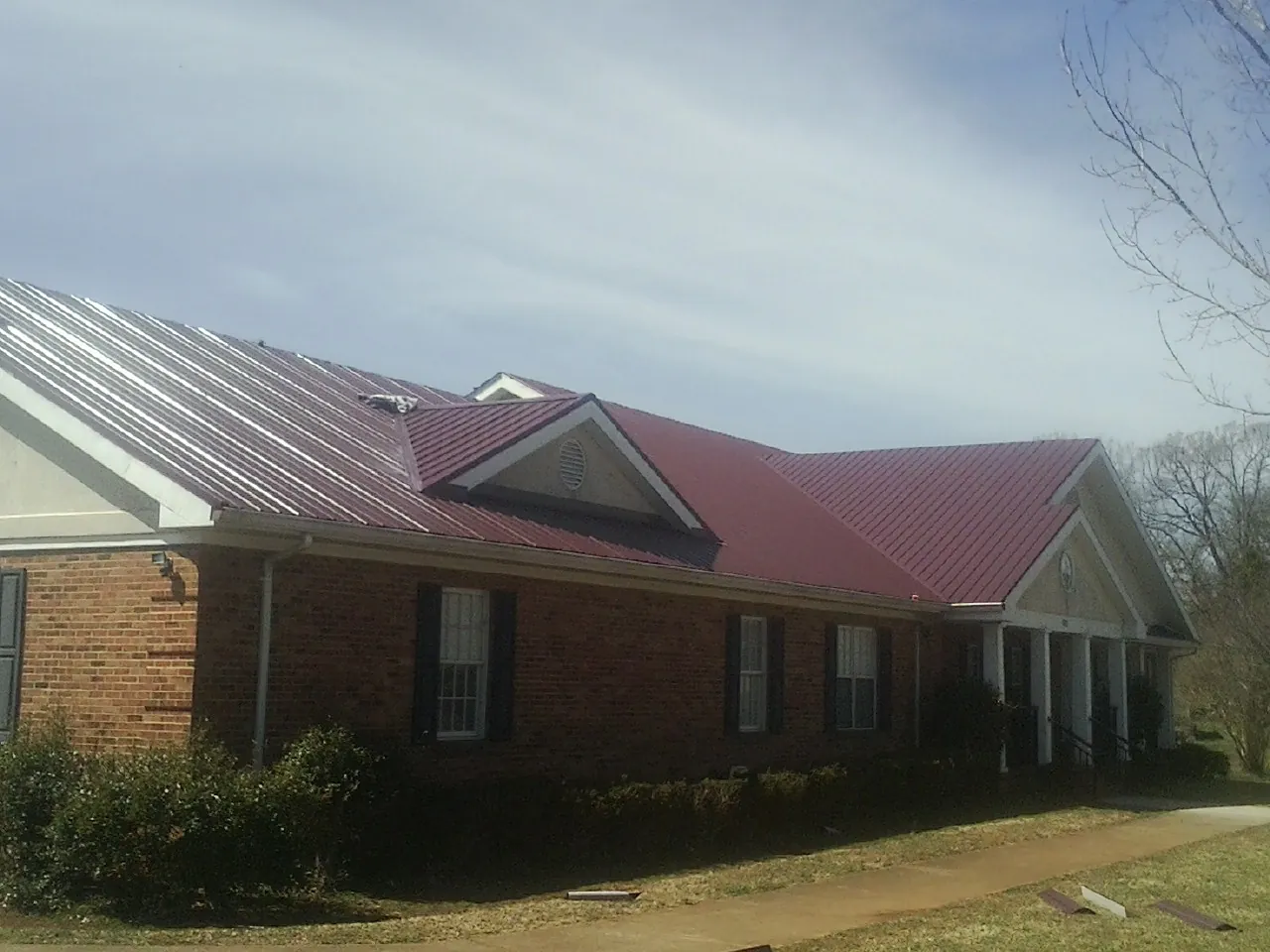 Red metal roof with gabled entries on a long brick building, from a Hail Damage Roof Repair job in Haworth