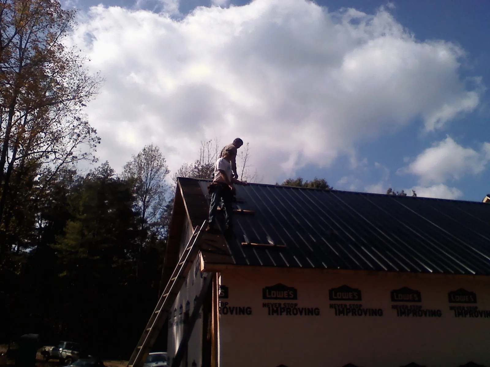 Roofer fastening dark metal panels high against a cloudy sky, from a Roof Inspection job in Haworth
