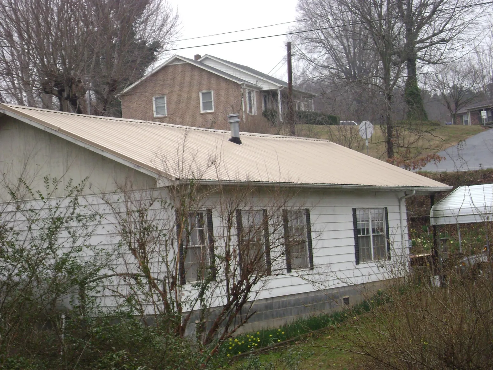 Tan metal roof on a white sided house set into a hillside — Commercial Roofing by Roofing Brothers in Haworth