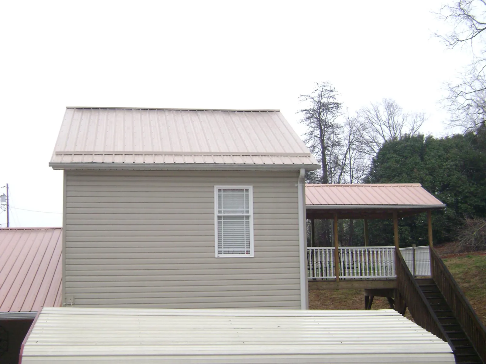 Tan metal roofs on a two story addition and attached porch, from a Roof Replacement job in Haworth